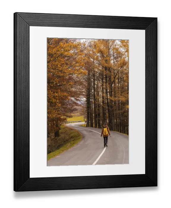 Framed Print : A young woman walking along a road surrounded by trees in autumn