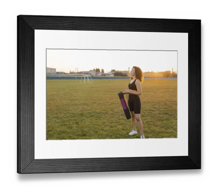 Framed Print : Woman with curly hair smiles while holding a yoga mat on a field