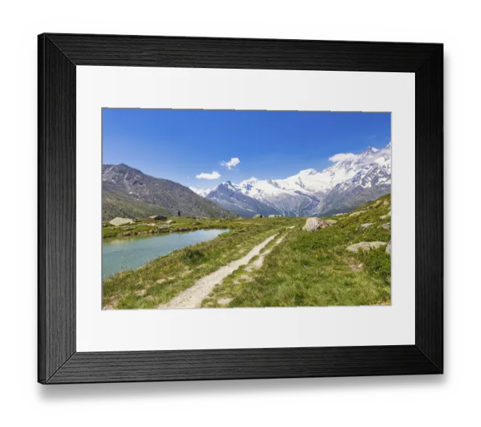 Framed Print : Hiking trail leads along a clear stream to snow-crowned mountains
