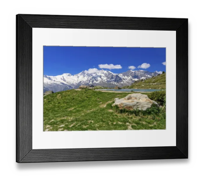 Framed Print : Green meadow with rocks in front of a snow-covered mountain panorama under a clear sky Framed Print : Green meadow with rocks in front of a snow-covered mountain panorama under a clear sky