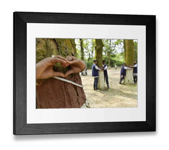 Framed Print : Hands forming a heart shape around a tree trunk with people in the background