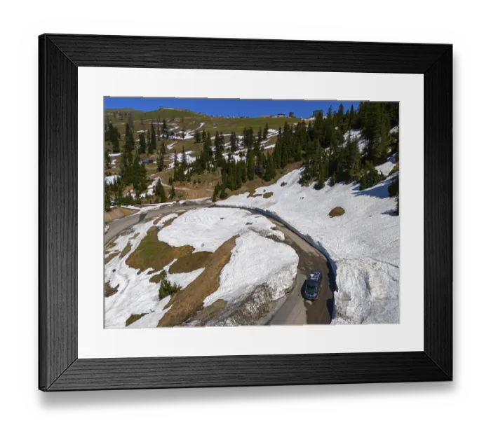 Framed Print : A winding road leads through a landscape of snow-covered hills and pine trees under a clear blue sky