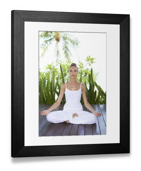 Framed Print : Beautiful serene woman meditating in the lotus position on a wooden deck with a backdrop of lush tropical vegetation