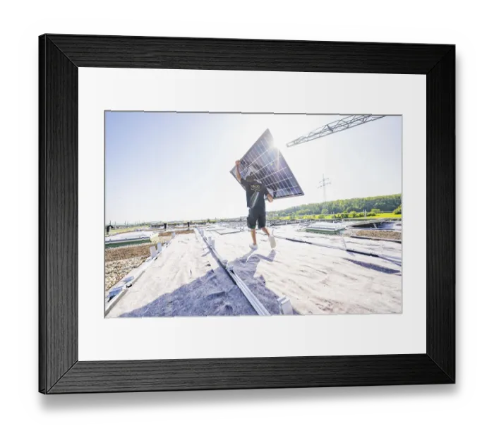 Framed Print : Worker carrying solar panel on an open roof in bright sunlight