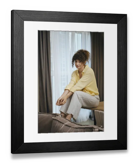 Framed Print : Cute woman with curly hair sits casually on a table in a well-lit room