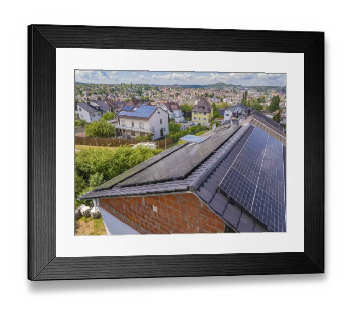Framed Print : Close-up of solar panels on a roof with a view of the city and green vegetation