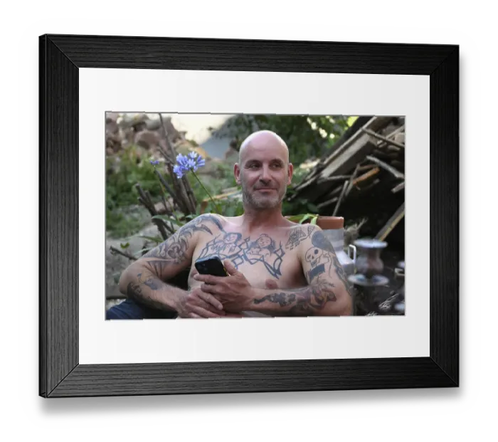 Framed Print : Young man with mobile phone, sitting in garden with bare upper body