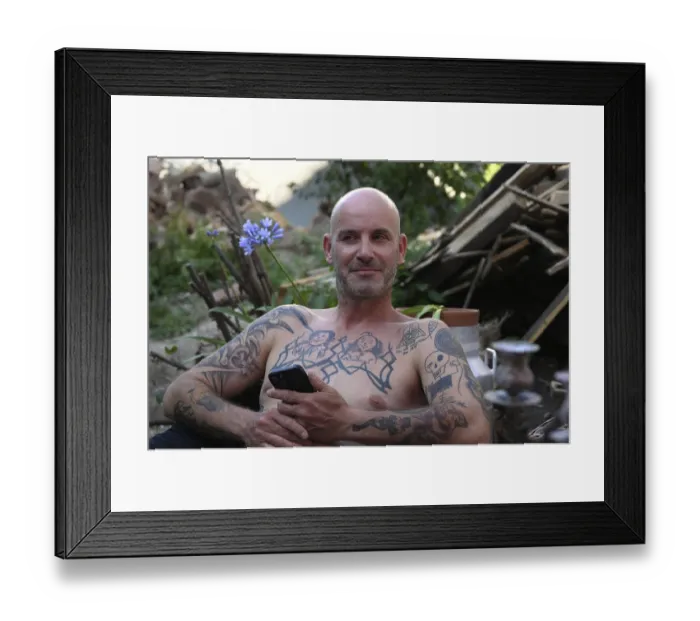 Framed Print : Young man with mobile phone, sitting in garden with bare upper body