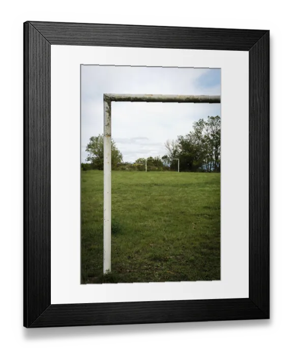Framed Print : Football goalpost in a grassy field under a cloudy sky near a rural area