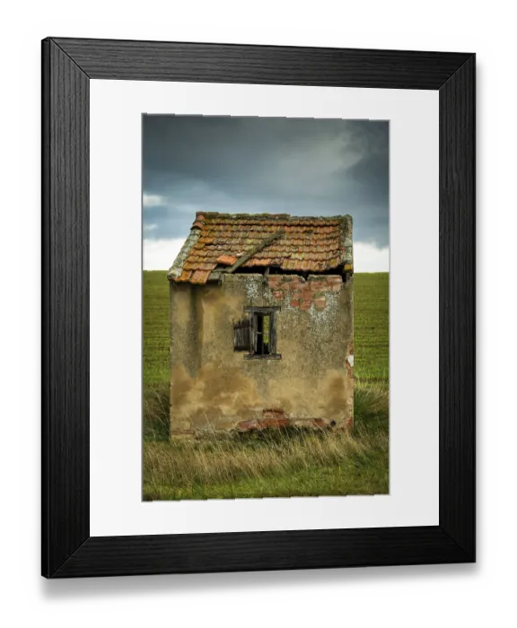 Framed Print : A small, dilapidated hut with a broken roof and cracked walls sits alone in a vast green field
