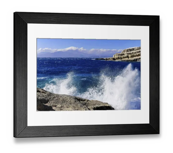 Framed Print : Bay, Matala beach, spray of waves crashing on rocks under a bright blue sky