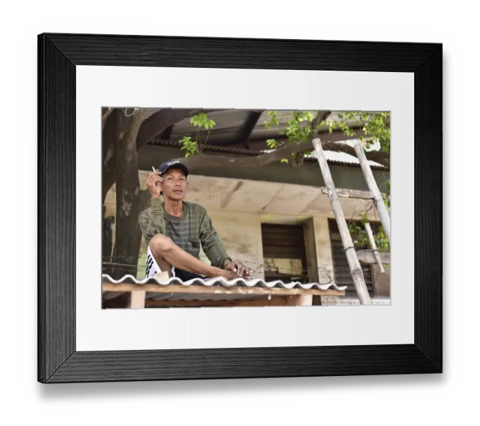Framed Print : Man sitting relaxed on a roof under a tree smoking a cigarette
