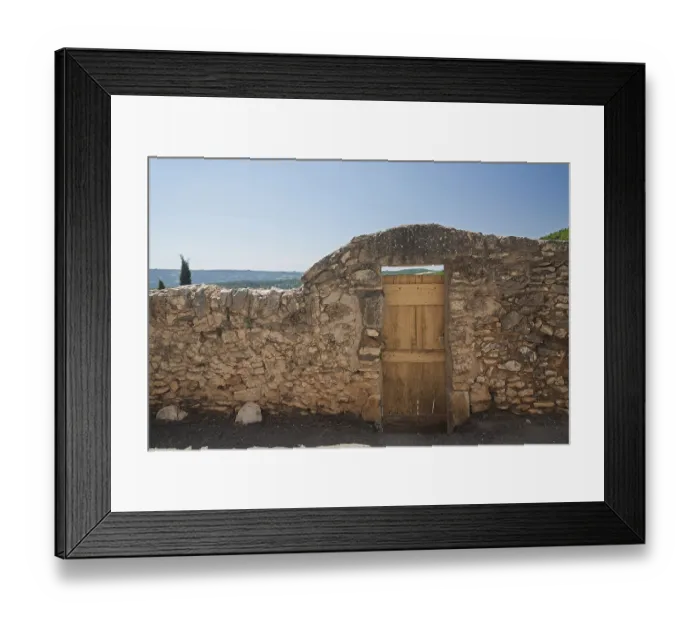 Framed Print : Stone wall with wooden gate and view of a wide landscape under a blue sky