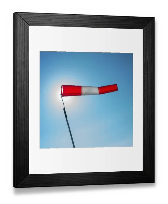 Framed Print : A vibrant windsock attached to a pole is fluttering in the wind against a clear blue sky