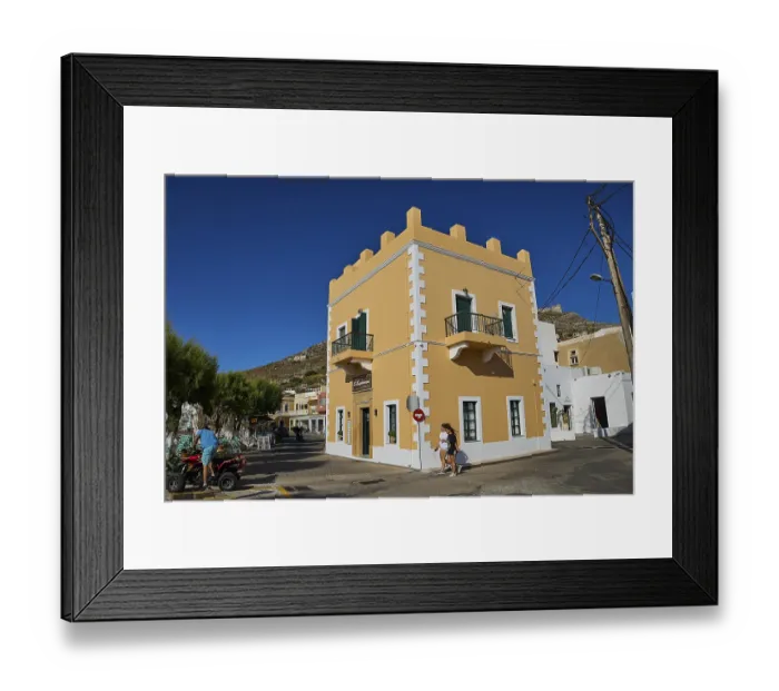 Framed Print : Mediterranean-style corner building with balconies and passers-by under a clear blue sky