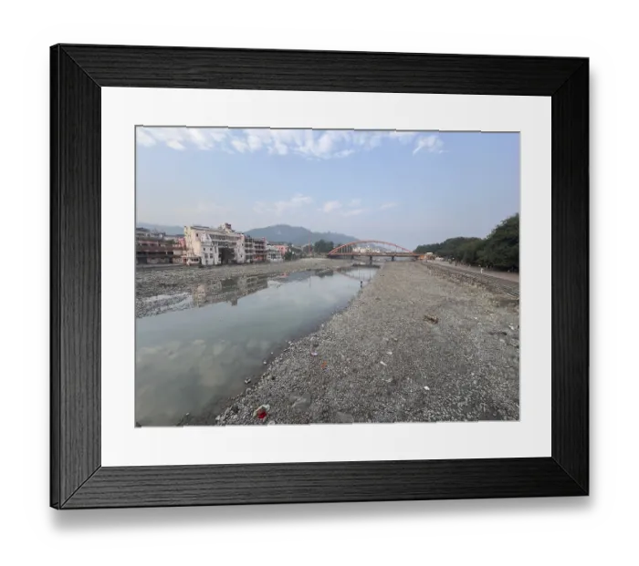 Framed Print : Empty riverbed with a bridge in the background and surrounding buildings under a cloudy sky