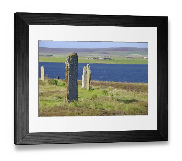 Framed Print : Ancient stones at the edge of a blue lake with green hills in the background