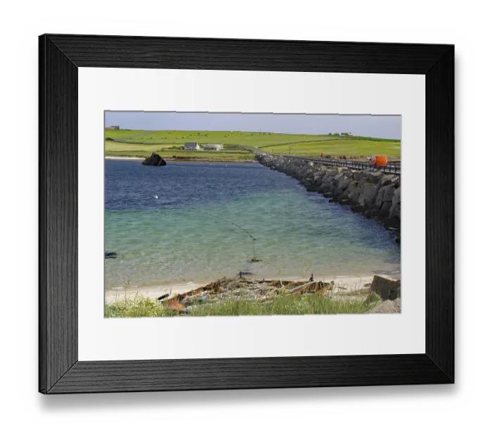 Framed Print : Ruin of a boat on the beach with a breakwater and green coastal background