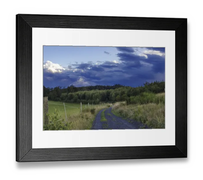 Framed Print : A rural path leads through a green landscape under a cloudy evening sky Framed Print : A rural path leads through a green landscape under a cloudy evening sky