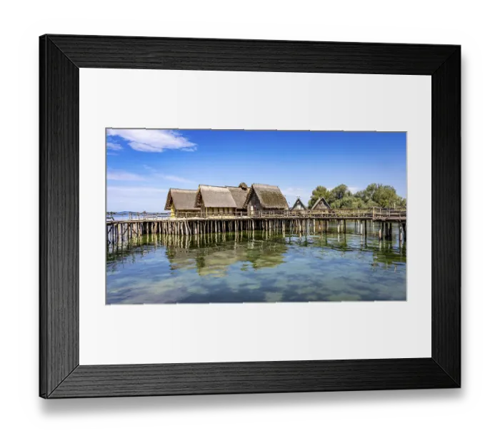 Framed Print : Historic pile dwellings on the shore of a lake with reflecting water