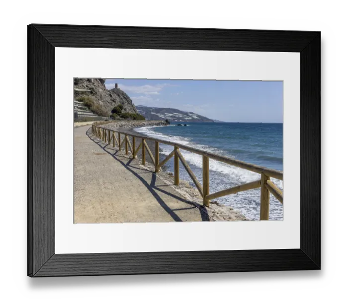 Framed Print : Promenade with wooden railings by the sea in front of the village with blue sky and sea