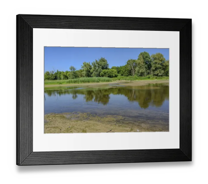 Framed Print : Landscape with a calm river and dense greenery under a blue sky