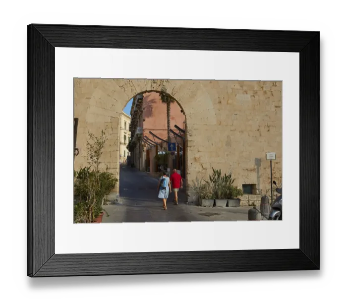Framed Print : People crossing a historic stone city gate surrounded by plants