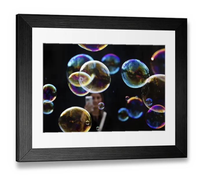 Framed Print : A woman photographs shimmering and floating soap bubbles against a black background Framed Print : A woman photographs shimmering and floating soap bubbles against a black background