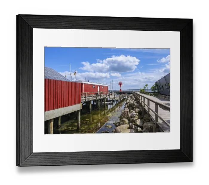 Framed Print : A red building on the waterfront with a jetty and rocks on the shore under a blue sky Framed Print : A red building on the waterfront with a jetty and rocks on the shore under a blue sky