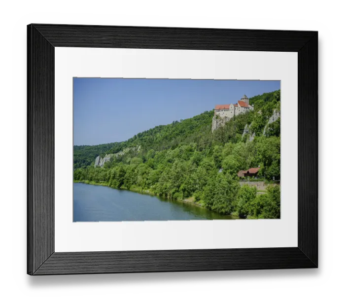 Framed Print : A castle towers over a river in the midst of a green forest and rocks