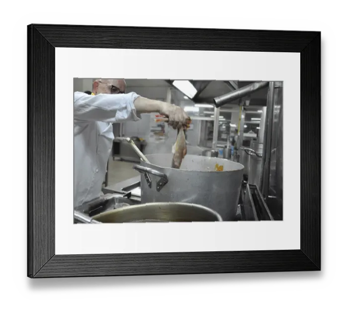 Framed Print : Chef holding fish over a steaming pot in a professional kitchen