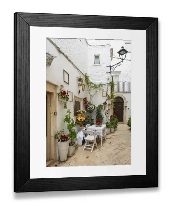 Framed Print : Narrow street with table and chairs in white town of Locorotondo