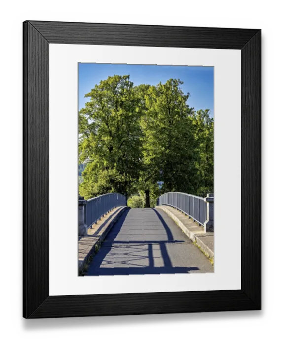 Framed Print : A quiet bridge with railings leads through green trees under a sunny blue sky