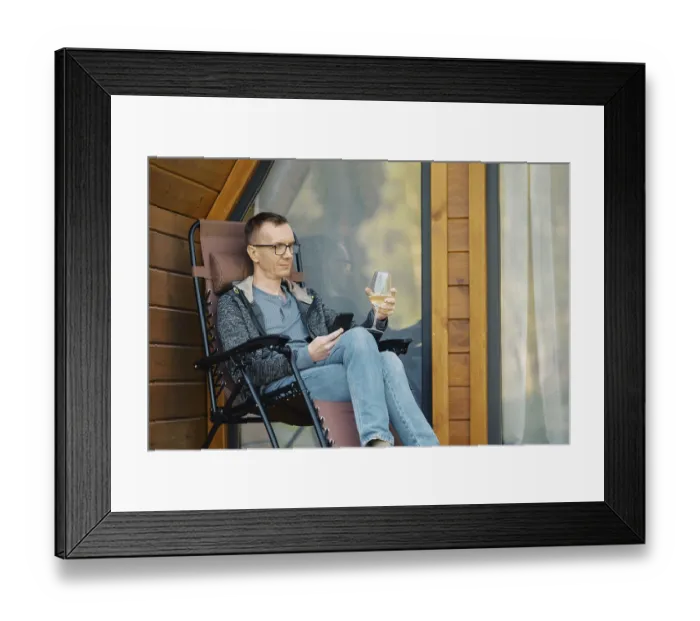 Framed Print : Middle-aged man looking at smartphone sitting on terrace of a house with a glass of wine