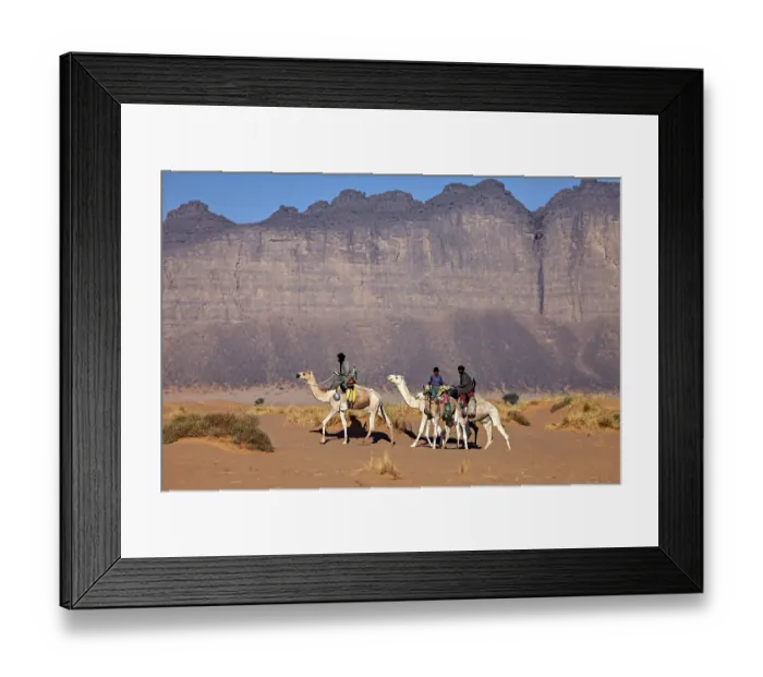 Framed Print : Three people riding camels through an arid desert landscape in front of imposing rock formations Framed Print : Three people riding camels through an arid desert landscape in front of imposing rock formations