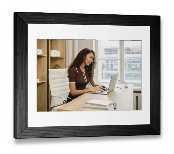 Framed Print : A woman with long curly hair is seated at a stylish wooden desk in a contemporary office Framed Print : A woman with long curly hair is seated at a stylish wooden desk in a contemporary office
