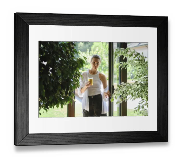Framed Print : A woman stands in a doorway holding a glass of refreshing beverage Framed Print : A woman stands in a doorway holding a glass of refreshing beverage