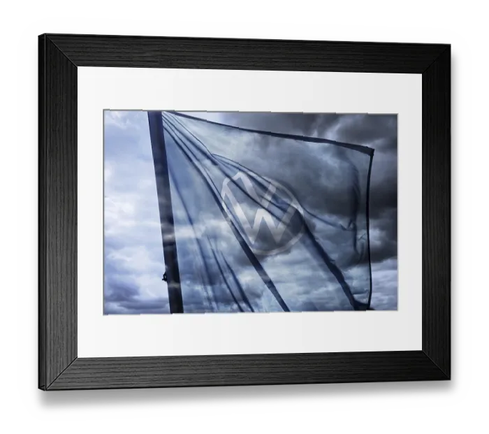 Framed Print : VW sign on the flag of a car dealer in front of a dark sky