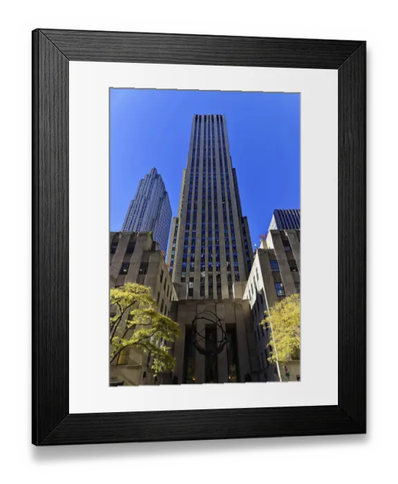 Framed Print : Architectural shot of a tall skyscraper against a blue sky with autumnal trees in the foreground