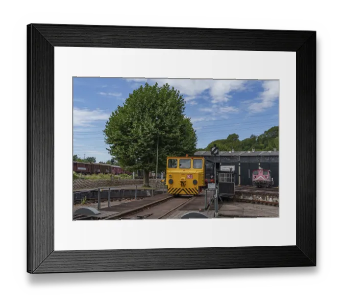 Framed Print : Yellow railway vehicle on rails in front of a tree and depot building