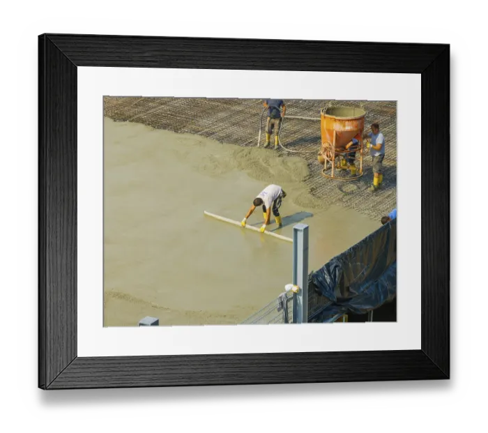 Framed Print : Workers smoothing concrete on a construction site while a concrete mixer stands in the background