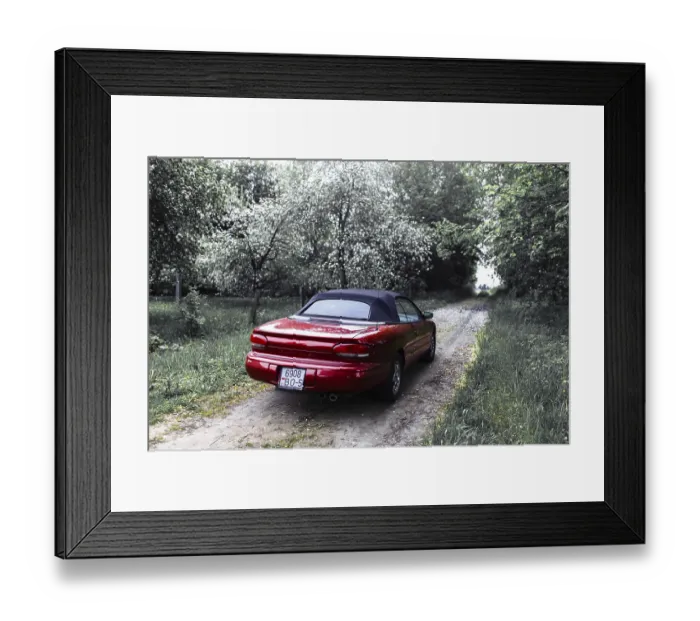 Framed Print : Red convertible car on a narrow path through dense forest with overcast skies