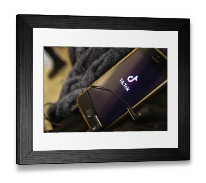 Framed Print : Smartphone displaying the TikTok app logo with tangled earbuds resting on it