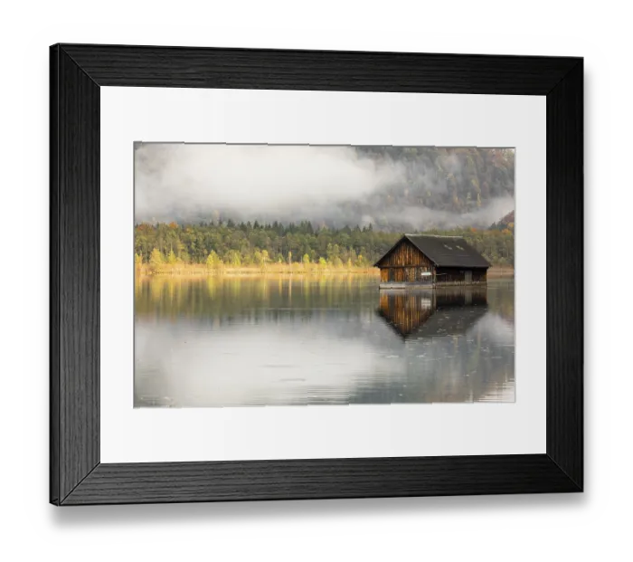 Framed Print : A boatshelter at lake Almsee. The forest in the background in full fall foliage and some fog above it