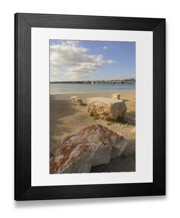Framed Print : Beach scene with large rocks and a sailboat visible across the calm water Framed Print : Beach scene with large rocks and a sailboat visible across the calm water