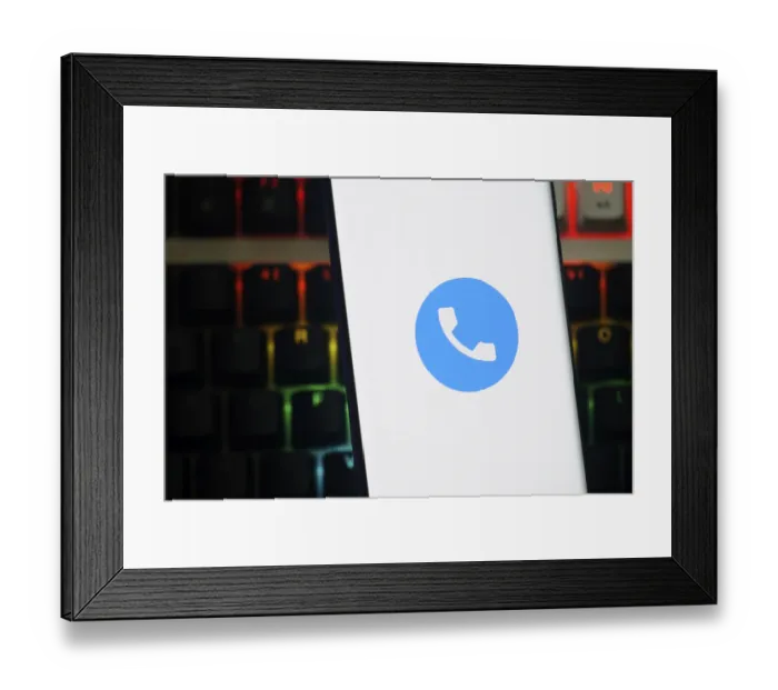 Framed Print : A smartphone displays a blue phone app icon against a white background over a colorful keyboard Framed Print : A smartphone displays a blue phone app icon against a white background over a colorful keyboard