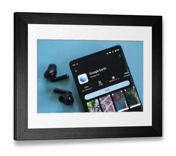 Framed Print : Google Earth app open on a phone with earbuds on a blue background