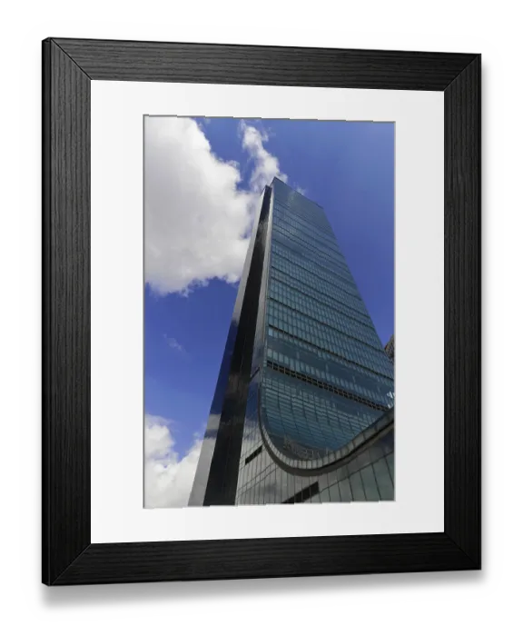 Framed Print : A tall modern office building with a glass facade under a blue sky