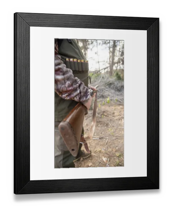 Framed Print : Hunter gripping a shotgun and wearing an ammunition belt while navigating through the dense forest Framed Print : Hunter gripping a shotgun and wearing an ammunition belt while navigating through the dense forest
