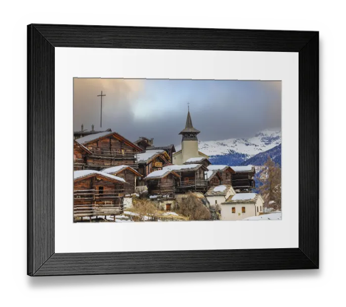 Framed Print : Old wooden houses with snow-covered roofs and the Saint Theodule church in the historic village centre